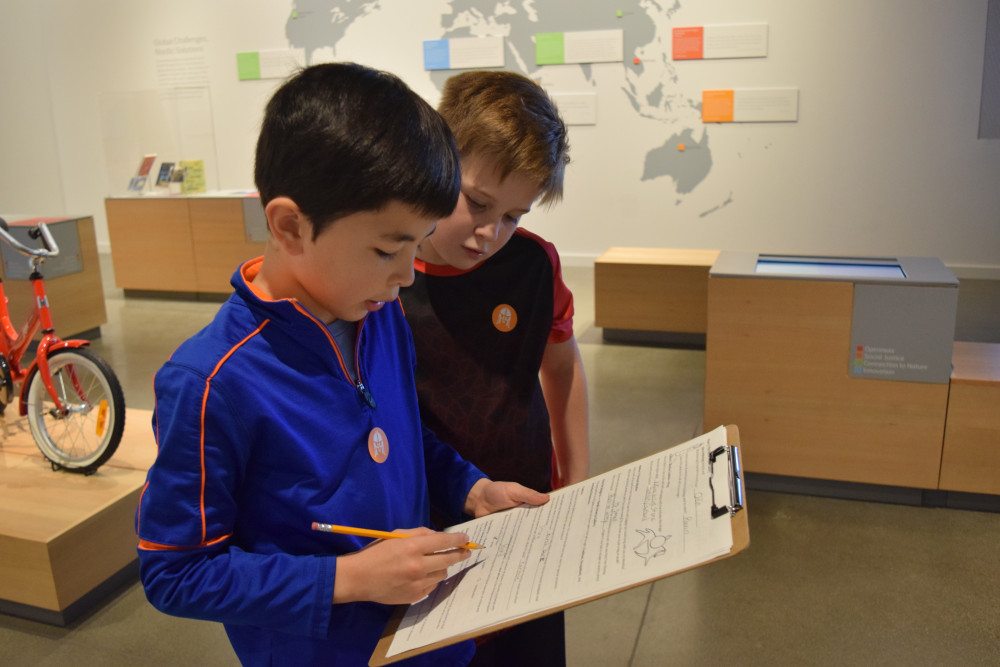 Two children hold a clipboard and complete a scavenger hunt in the Nordic Journeys exhibition.