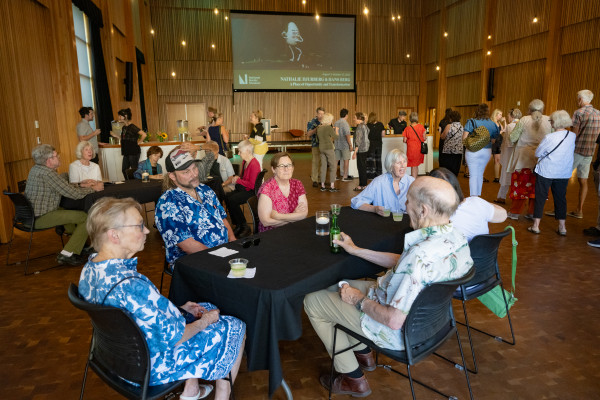 A group of people mingles at a table in Osberg Great Hall, while others line up behind them for drinks at a bar set up for the event.