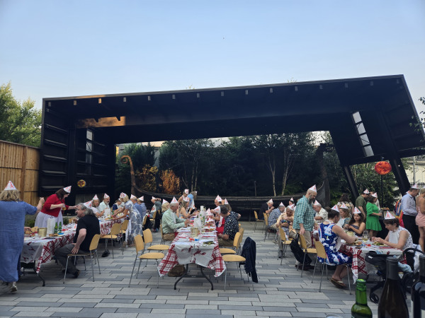 Several long tables are lined up for a dinner party in front of a wooden boat displayed in the Museum's East Garden.