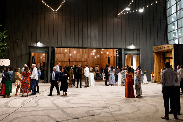 A group mingles at standing tables on the Fishermen's Sun Terrace at nighttime, with overhead string lights lit up against the dark sky.