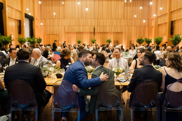 A couple kisses during their reception in Osberg Great Hall, against the hemlock walls and with pendant lights shining above.